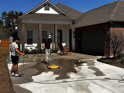 Crew cleaning a concrete driveway with a surface cleaner, showing clean and dirty sections