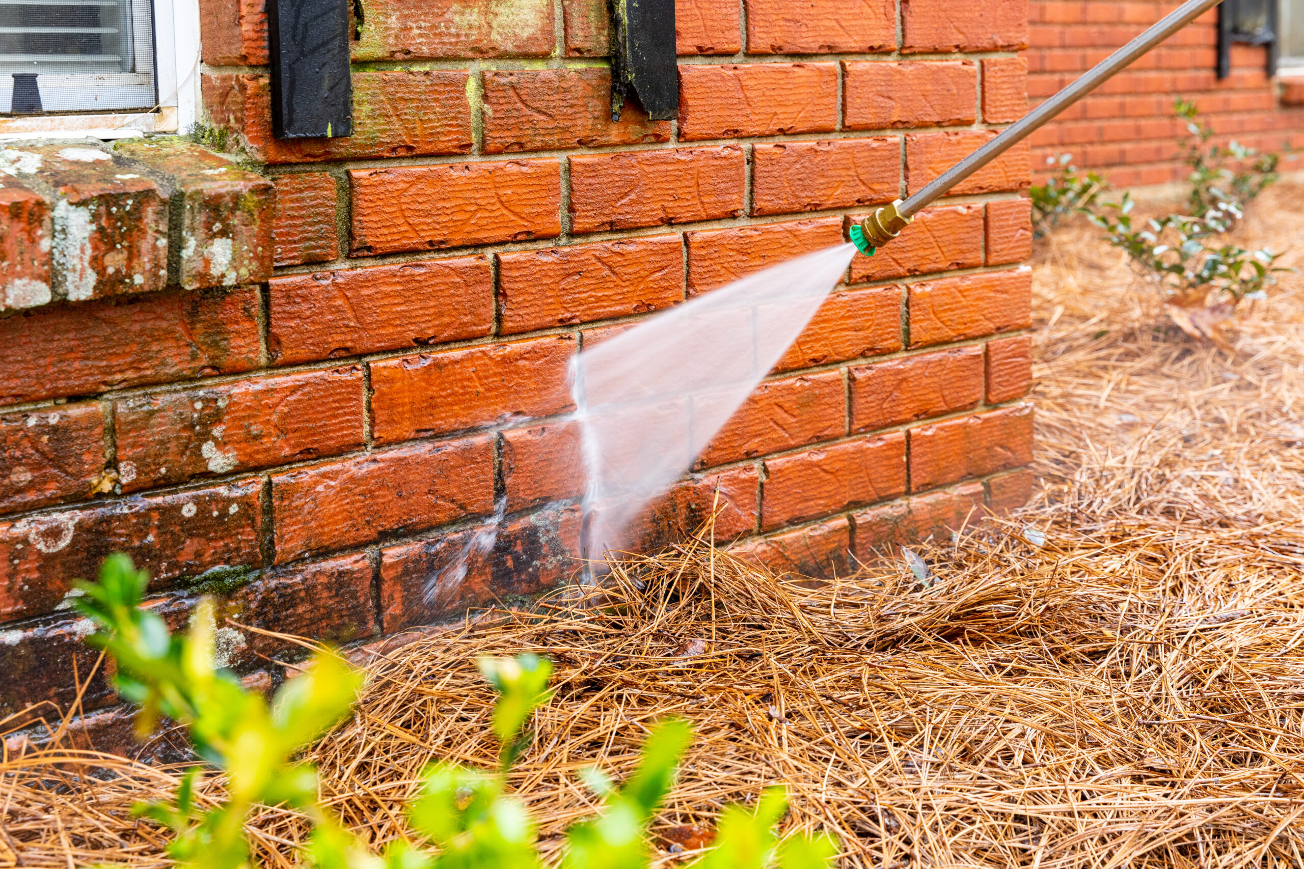 Dirty brick wall being cleaned with a pressure washer.